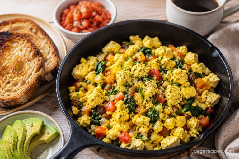 Golden tofu scramble with red bell pepper, spinach and chives in a cast-iron skillet, served with toast, avocado and salsa