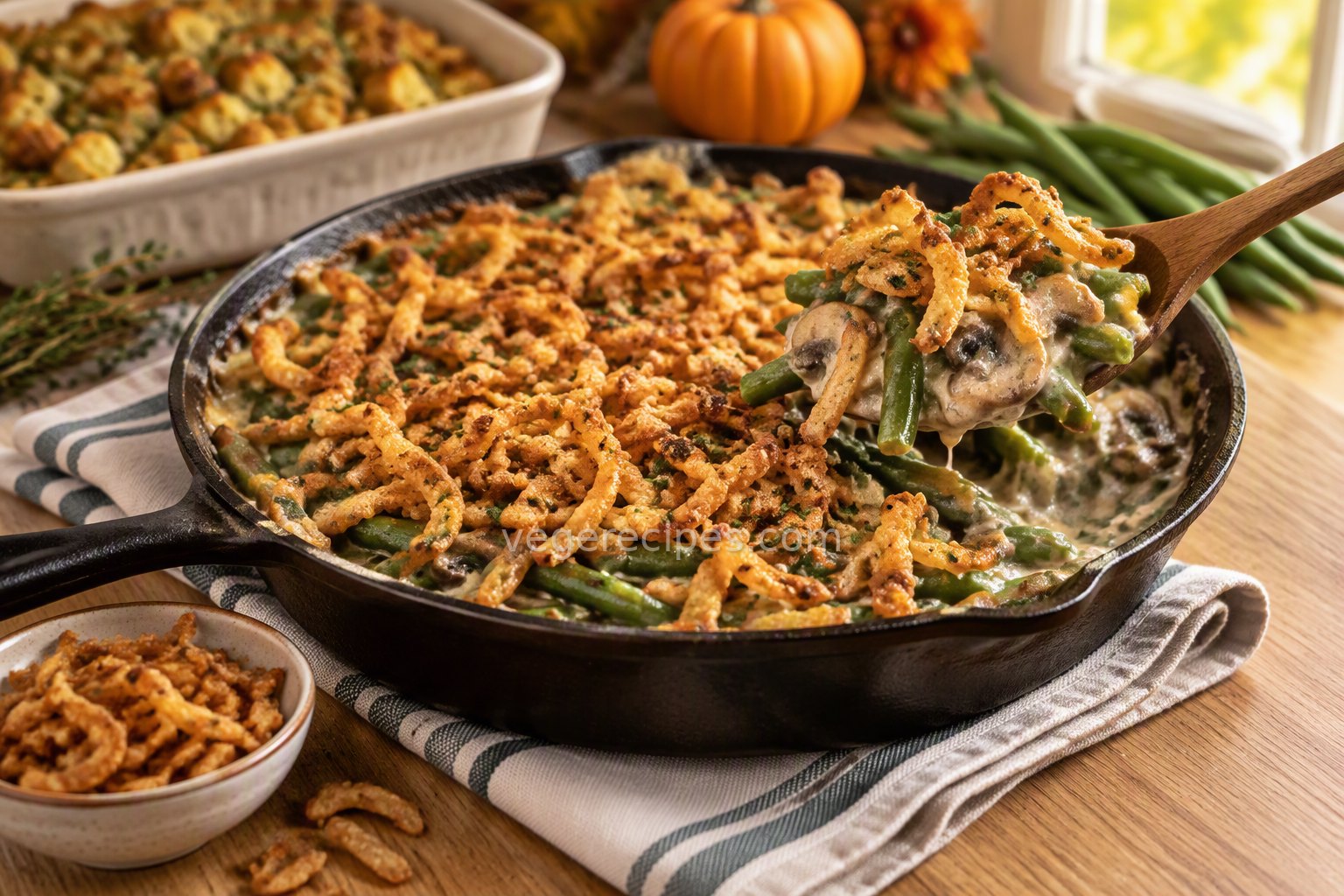 Cast-iron skillet of green bean casserole with a creamy mushroom sauce and a golden crispy onion topping, with a spoonful lifted out