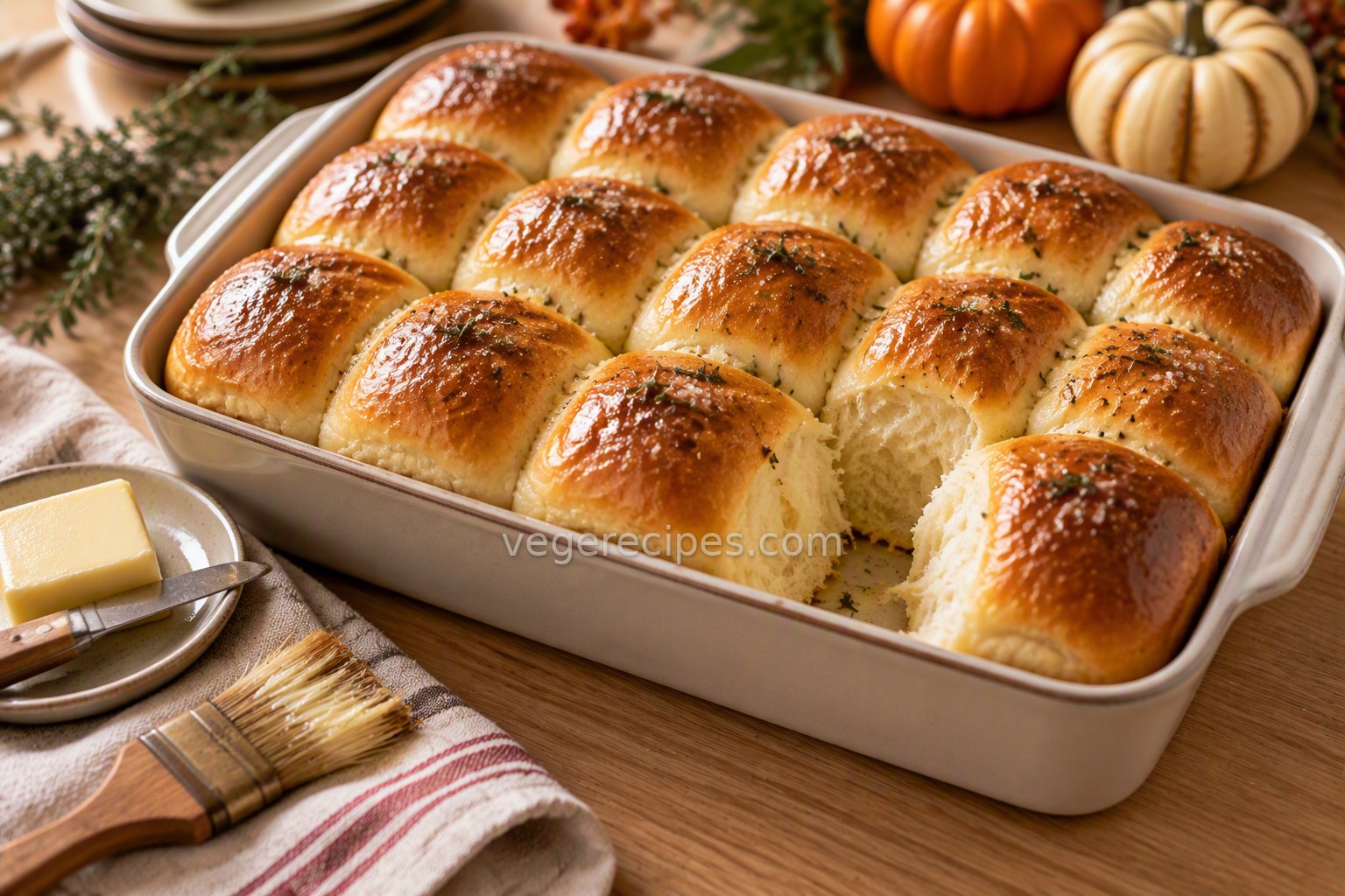 Baking dish of golden pull-apart dinner rolls brushed with butter and flecked with herbs, one roll pulled away to show the fluffy inside